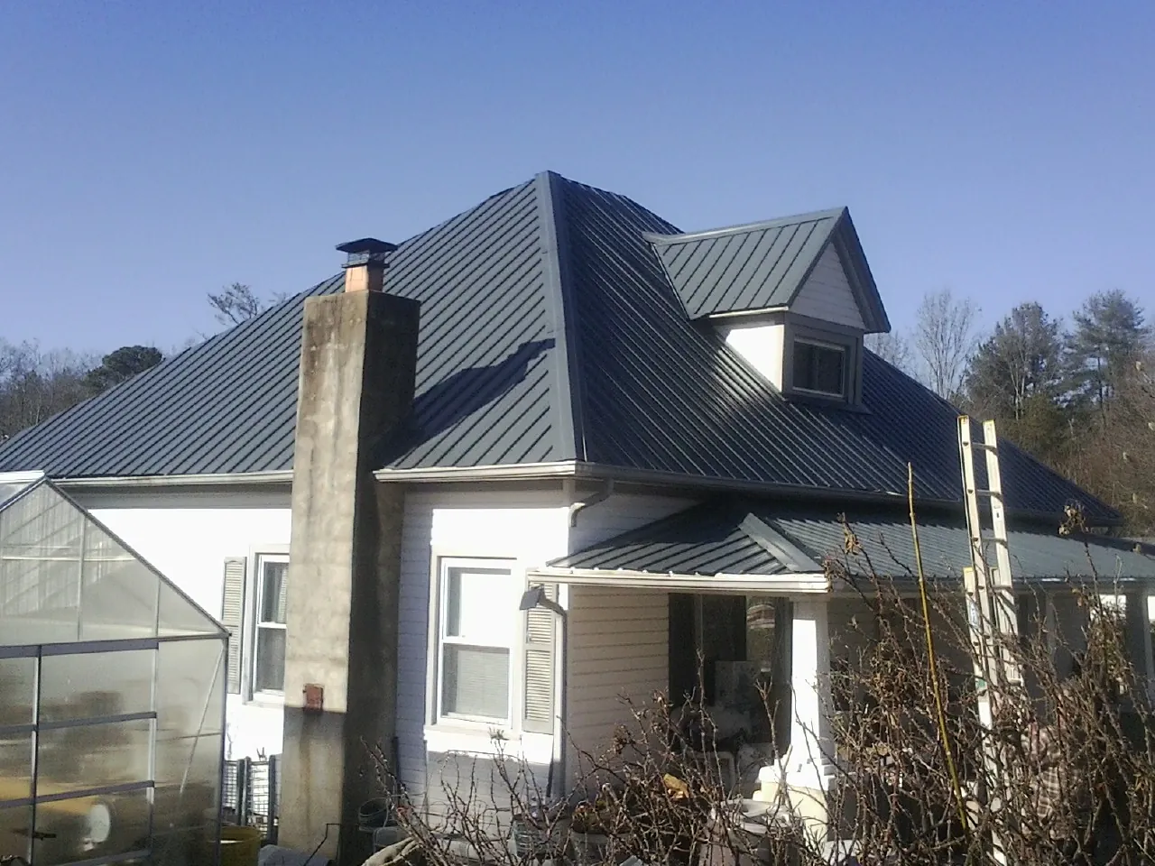 Dark blue standing seam metal roof on a white farmhouse with dormer — Slate & Tile Roof Repair by Roofing Brothers in Menlo