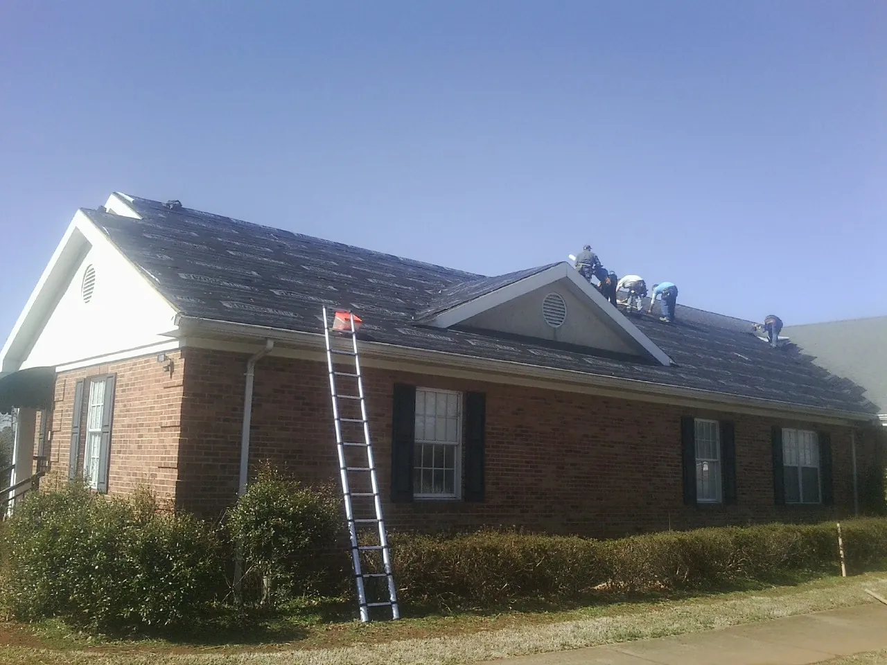 Crew tearing shingles off a brick ranch roof with a ladder set — Metal Roof Repair work by our crew in Menlo
