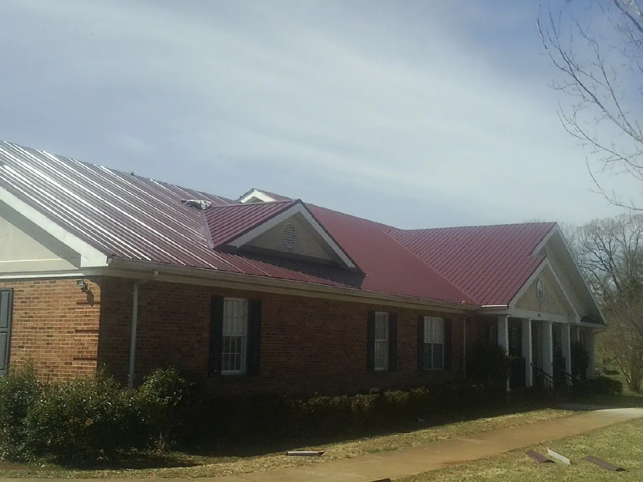 Red metal roof with gabled entries on a long brick building, from a Hail Damage Roof Repair job in Menlo