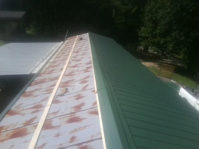 Old rusted panels beside newly installed green metal roofing — Wind Damage Roof Repair by Roofing Brothers in Menlo