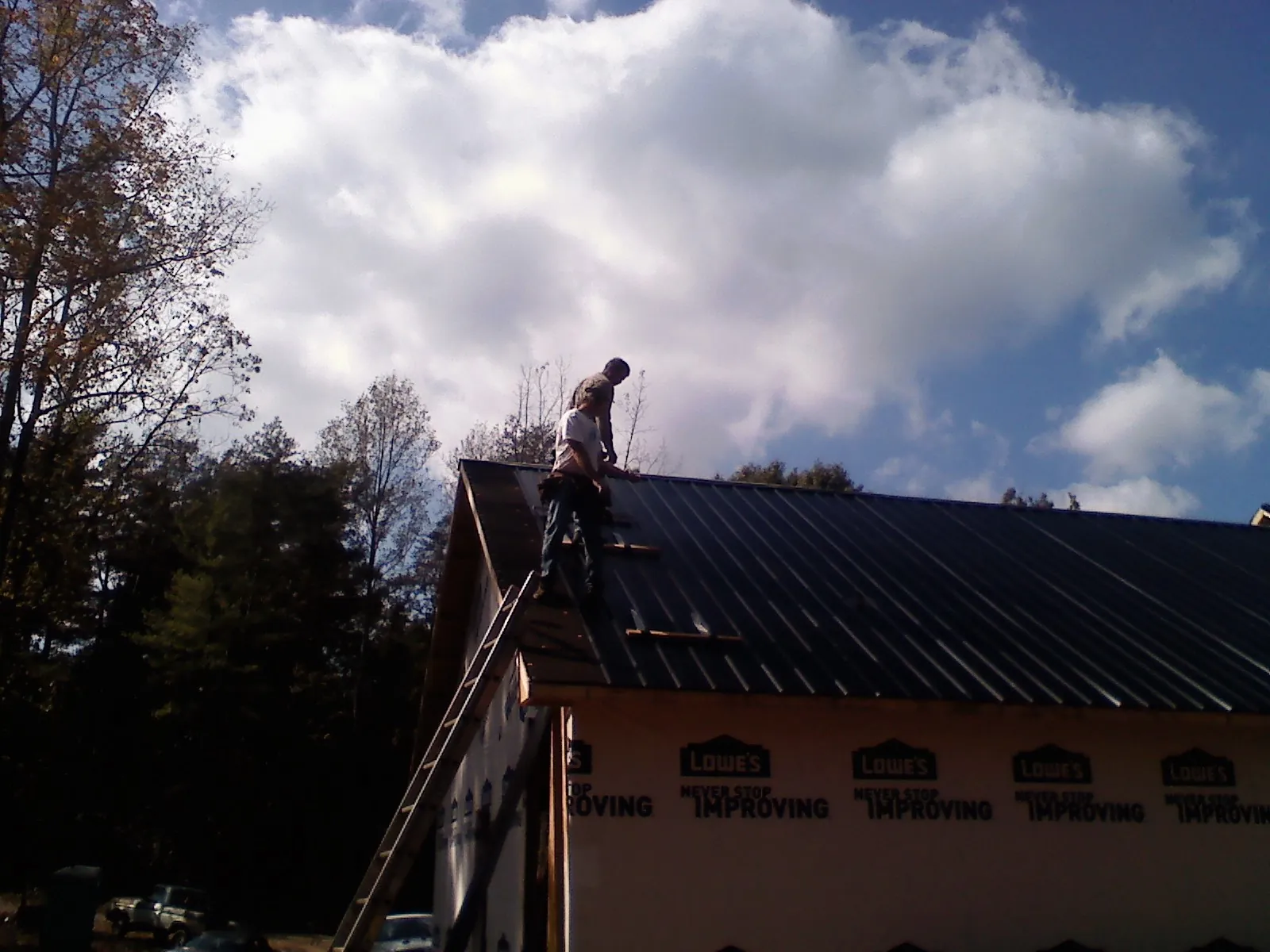Roofer fastening dark metal panels high against a cloudy sky, from a Roof Inspection job in Menlo
