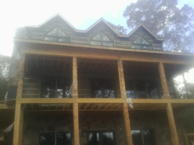Dormers and porch framing on a large log home under construction — Roof Coating work by our crew in Menlo