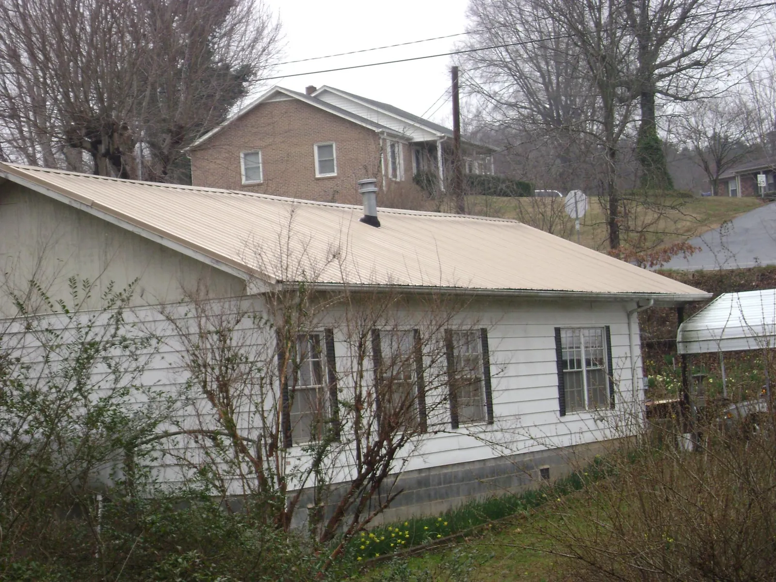 Tan metal roof on a white sided house set into a hillside — Commercial Roofing by Roofing Brothers in Menlo